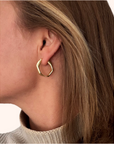 Gold hoop earring worn by a person with a neutral background