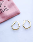 Gold hoop earrings on a white surface with a pink pouch labeled 'tuuli' in the background.